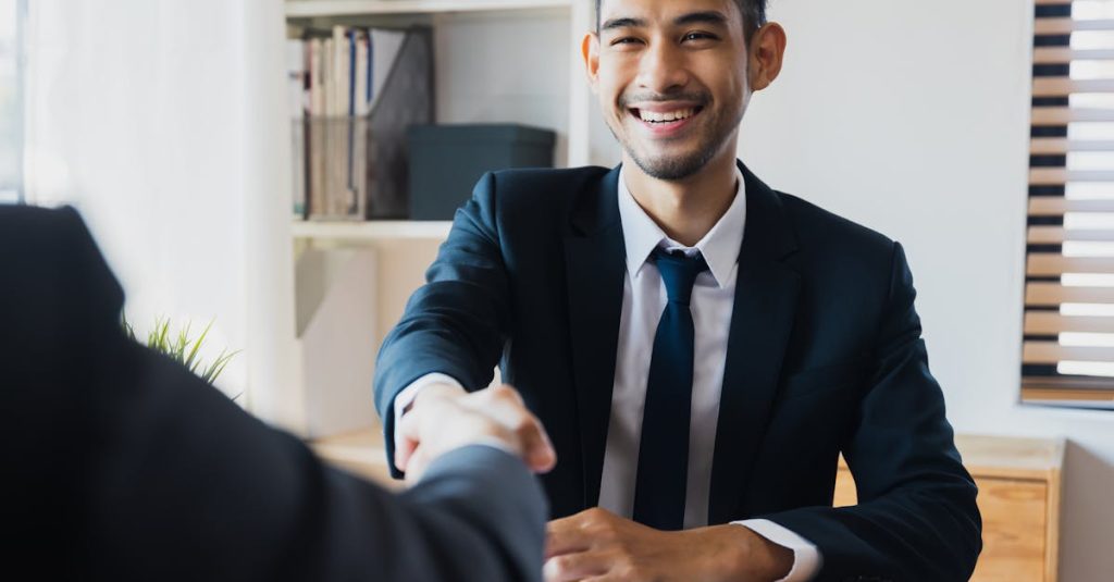 Confident businessman in suit shaking hands at office desk, symbolizing successful partnership.