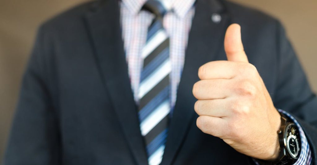 Close-up of a businessman in a suit giving a thumbs up gesture, symbolizing success.