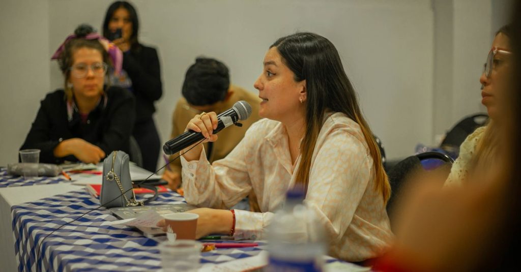 Woman participating in a group discussion, holding a microphone at a table indoors.