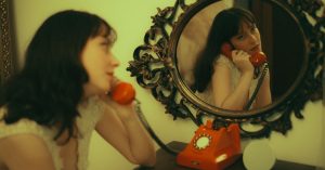 Artistic vintage-style photo of a woman using an orange rotary phone in the mirror.