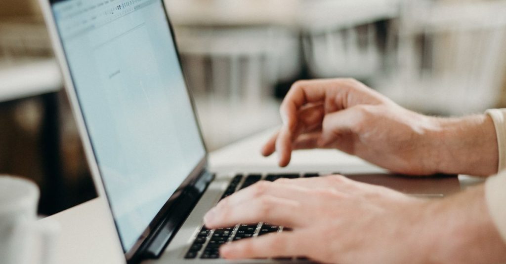 Close-up of hands typing on a laptop in a cozy indoor cafe setting.