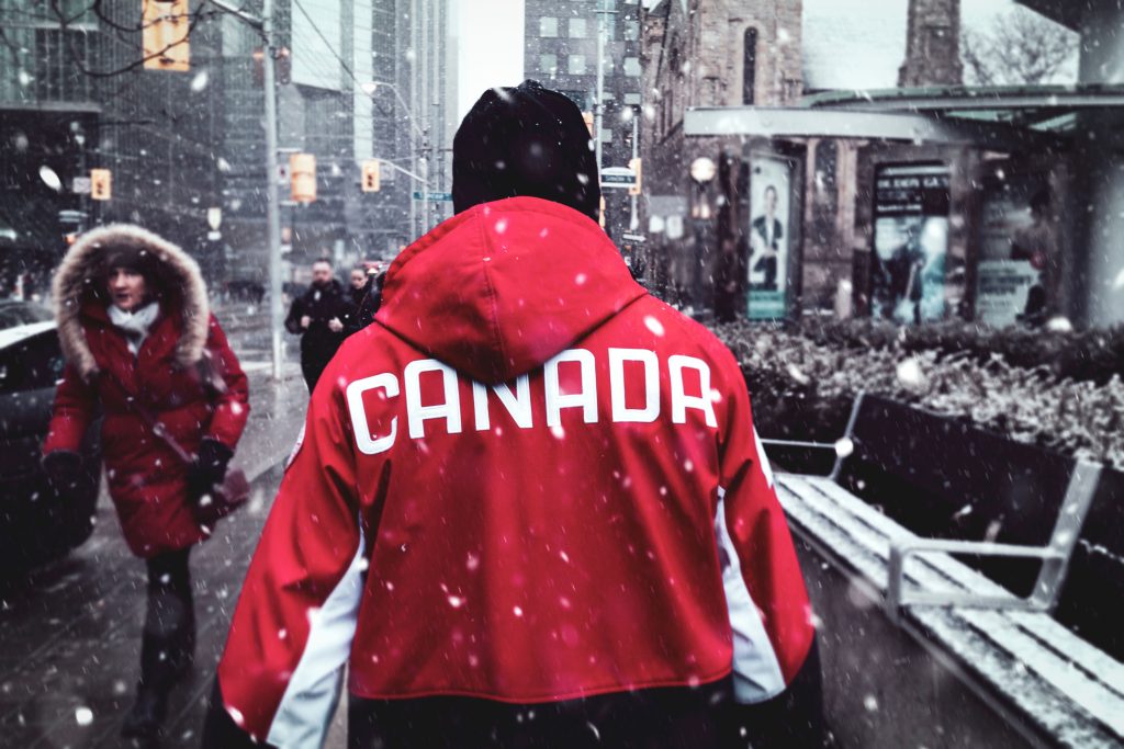 A man in a red Canada jacket walks through snowy downtown Toronto during winter.