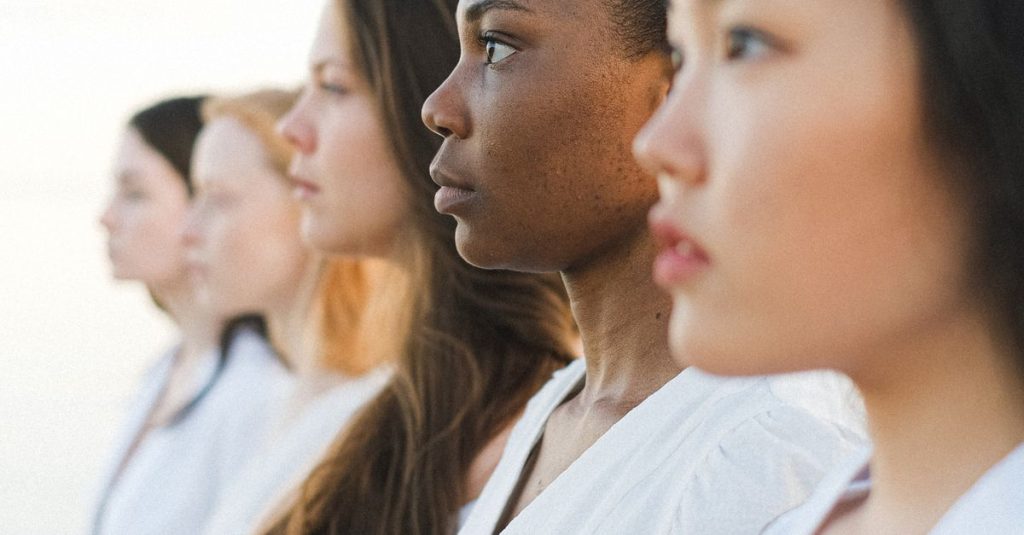 Five diverse women in white outfits standing side by side, symbolizing unity.