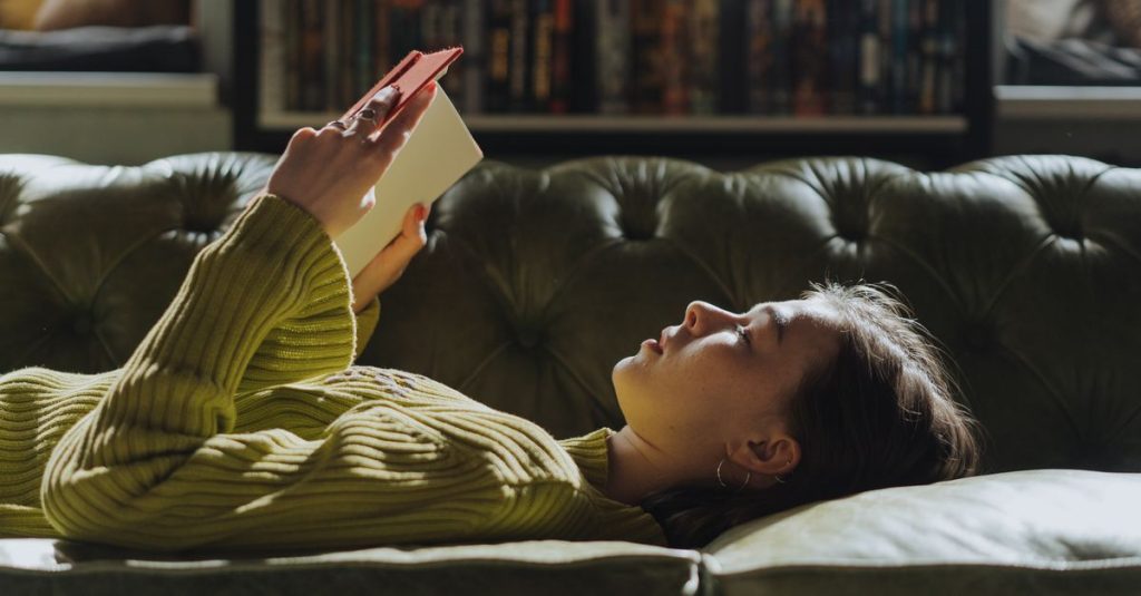 A young woman lies on a sofa reading a book, enjoying a peaceful indoor moment.
