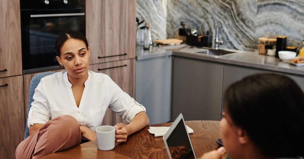Two women engage in a thoughtful conversation at a round kitchen table, creating a warm and inviting atmosphere.