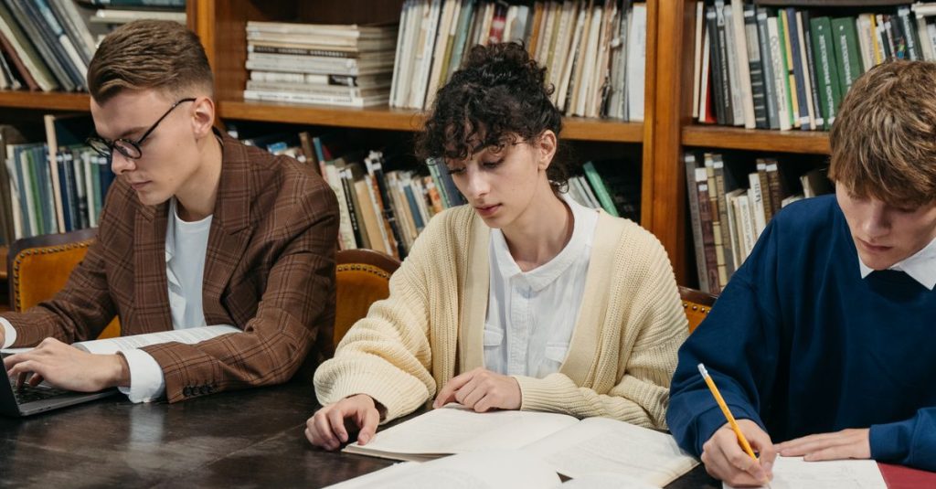 Students focused on studying in a university library filled with bookshelves.