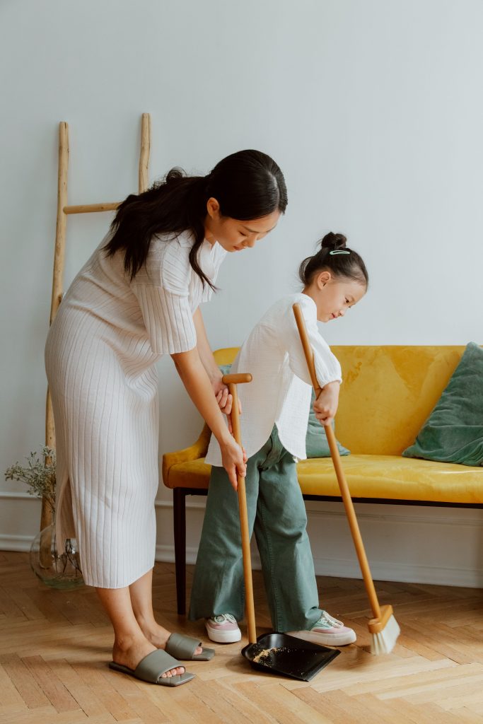 A mother and daughter enjoying quality time sweeping the living room.