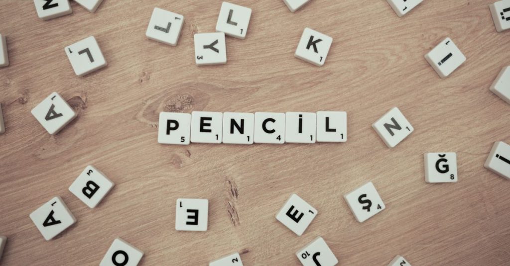 Wooden surface with scattered Scrabble tiles forming the word 'Pencil'.