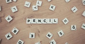 Wooden surface with scattered Scrabble tiles forming the word 'Pencil'.