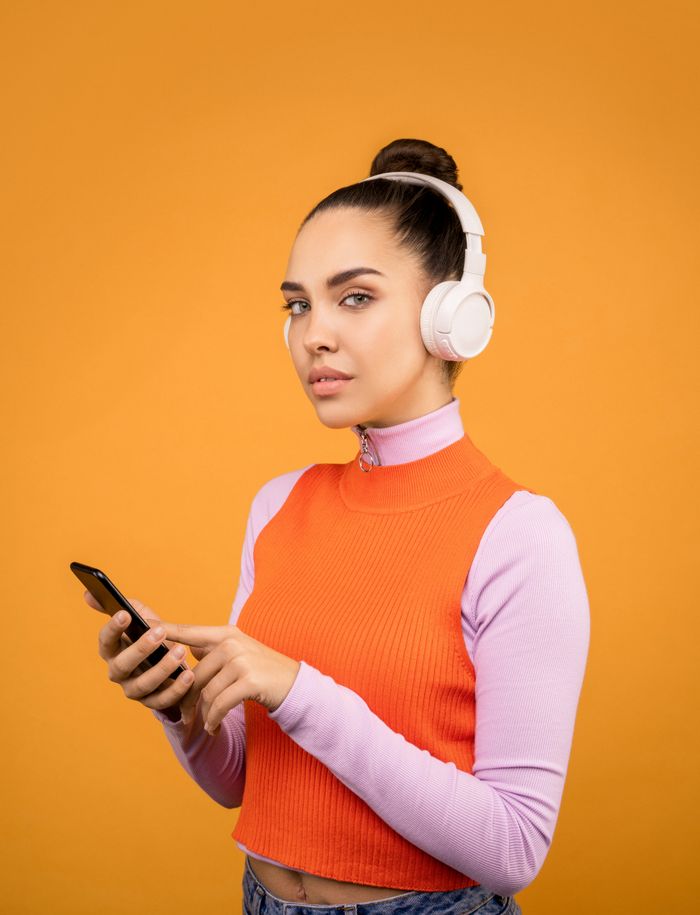 Fashionable woman in headphones using smartphone against an orange background.
