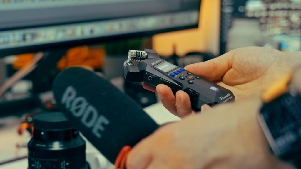 Detailed image of hands holding a microphone and recorder in a studio environment.