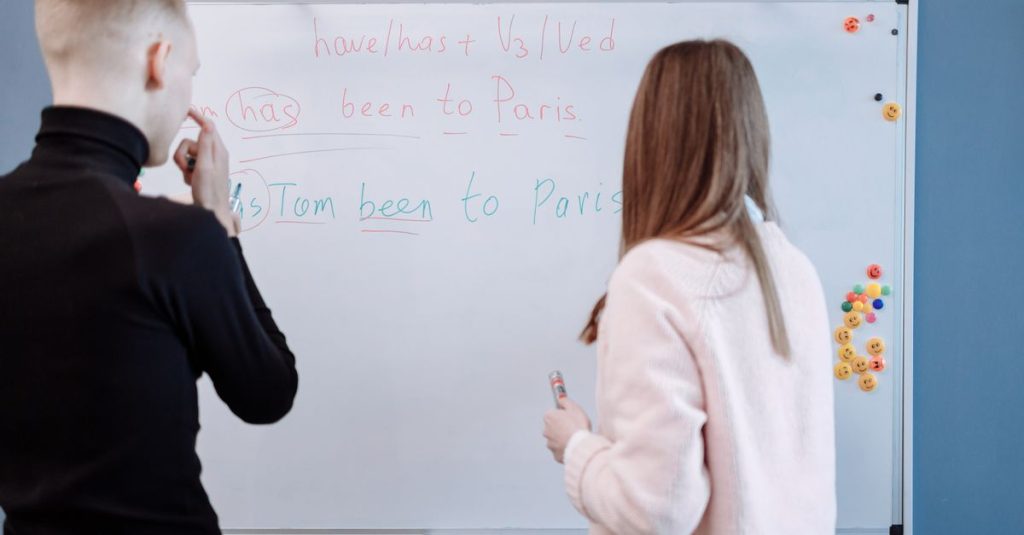 Two students studying English grammar at a whiteboard in a classroom setting.