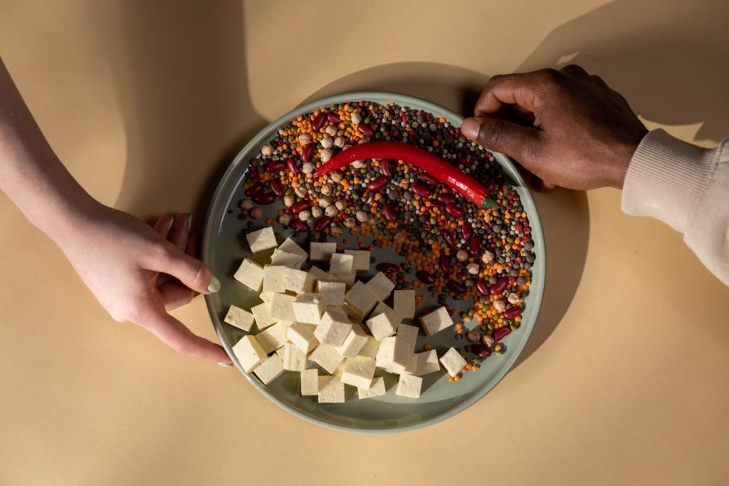 A diverse plate with tofu, legumes, and a chili pepper. Hands shown.