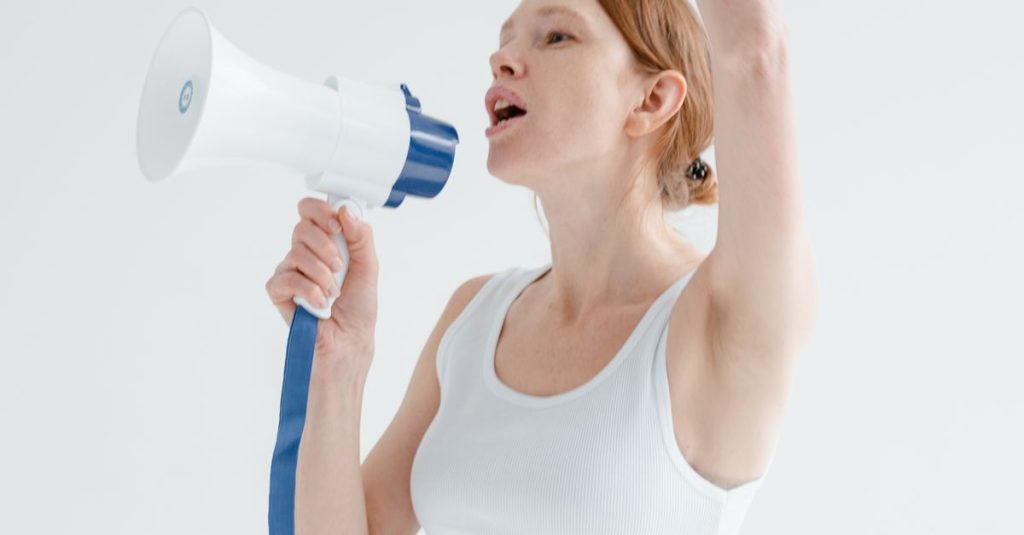 Woman raising arm and shouting into megaphone indoors, white background.
