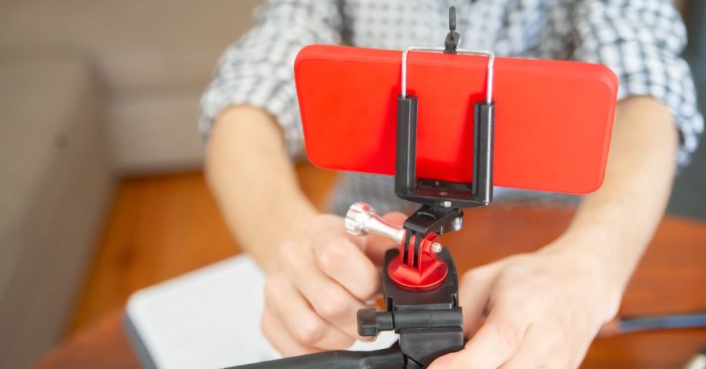 Close-up view of a person setting up a smartphone on a tripod indoors.