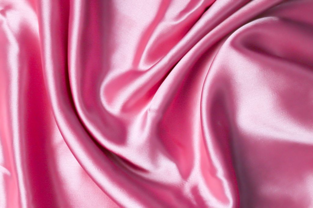 A close-up view of pink satin fabric showcasing its smooth, lustrous texture. Perfect for design projects.