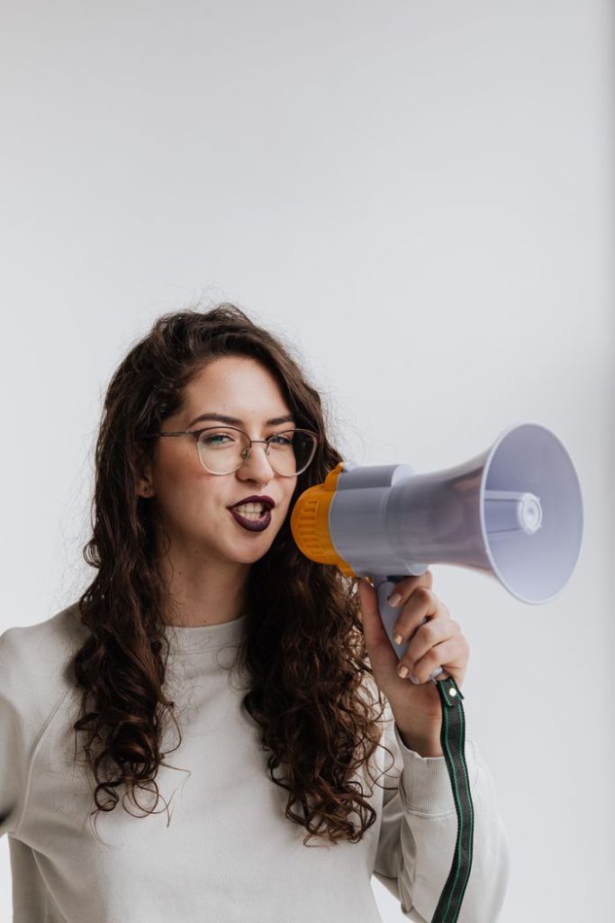 Confident woman with curly hair speaking into a megaphone indoors, expressing her voice.