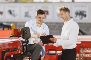 Two men discussing tractor purchase, collaborating outdoors with clipboard.