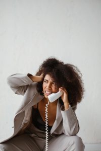 Stressed African American woman with afro hairstyle sitting and holding a phone to her ear indoors.