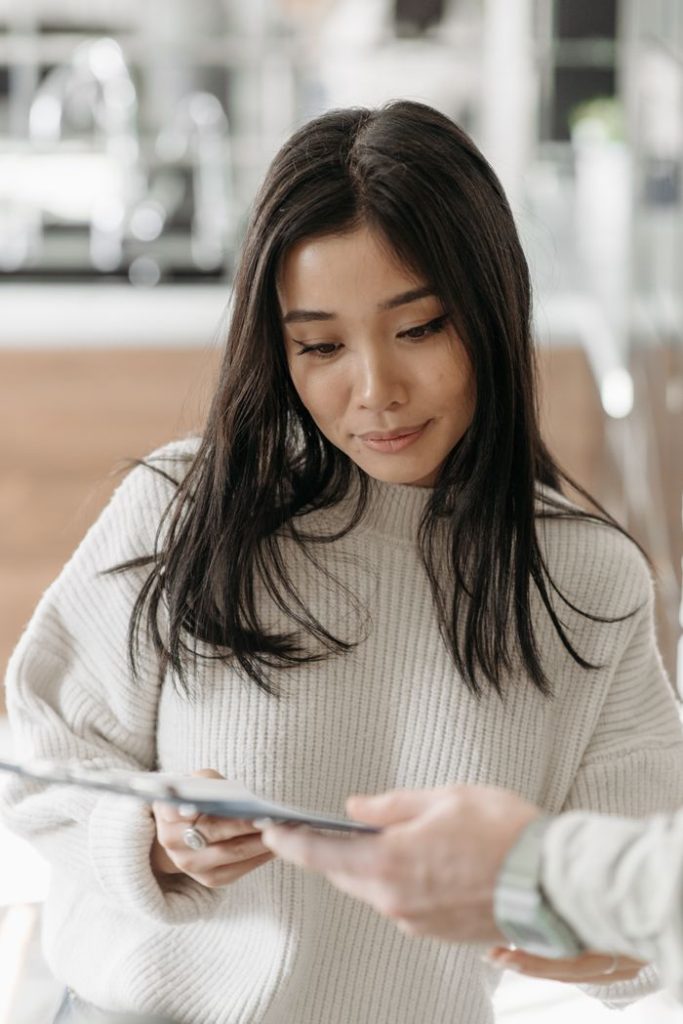 Asian woman reading a delivery form indoors. Captures the essence of home delivery and online shopping.