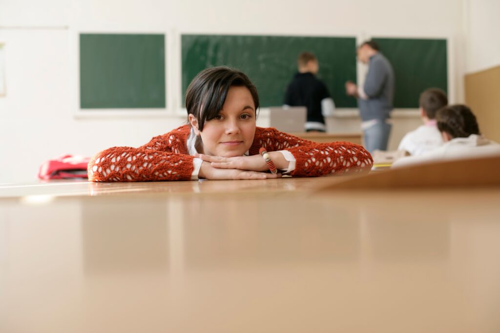 A young student rests her head on a desk in a classroom, with a focus on education and relaxation.