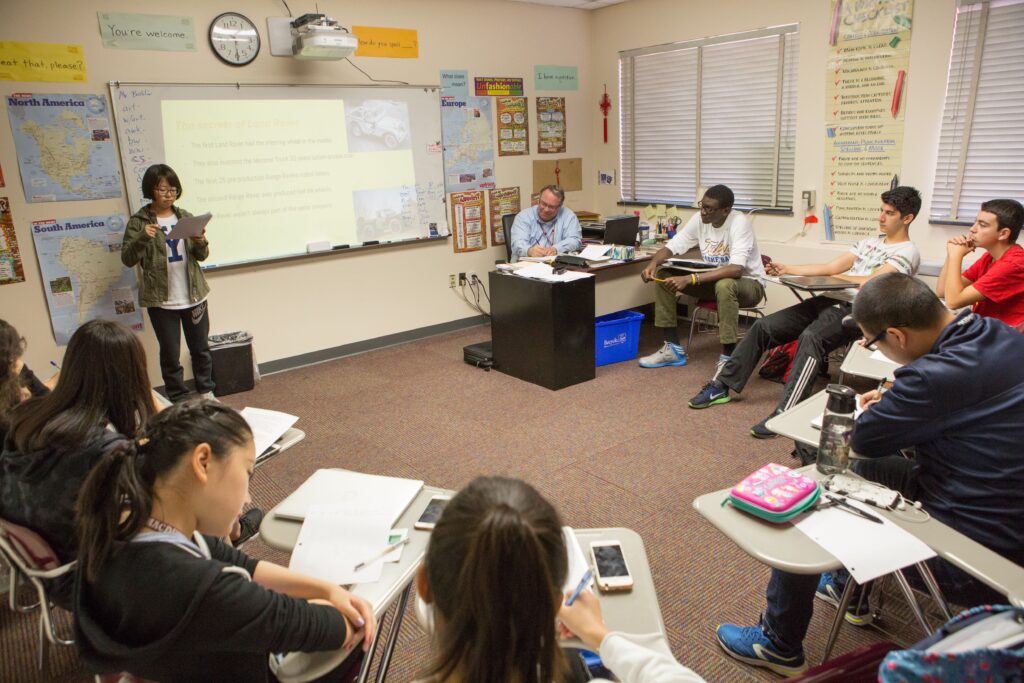 A diverse group of students in a classroom participating in a lesson with an educator.